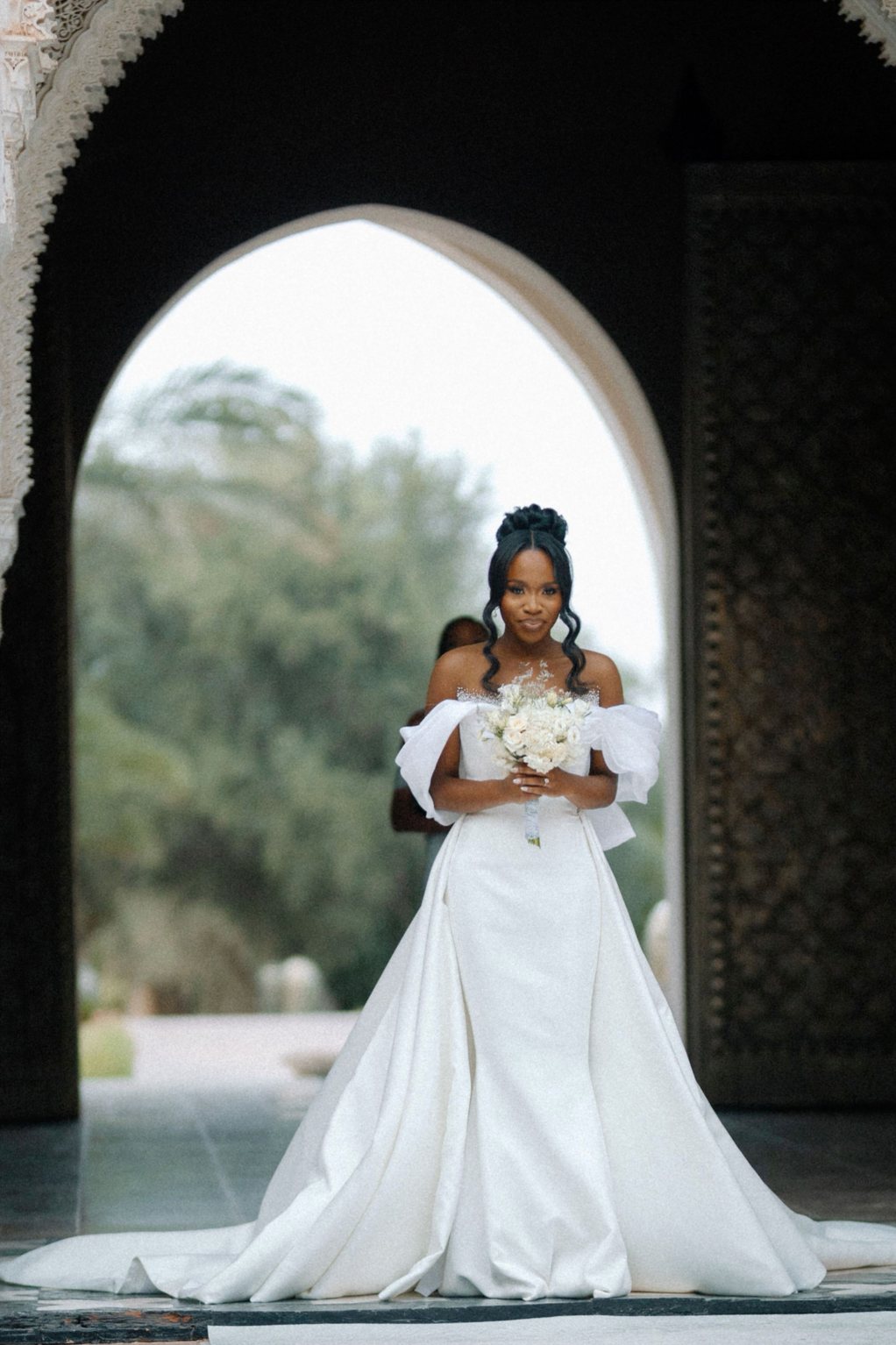 Zainab with her bouquet beneath a carved Moorish arch, Marrakech
